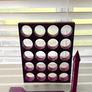 Puede incluir: Una rejilla rectangular de color morado oscuro con veinte recortes circulares dispuestos en cuatro filas y cinco columnas, acompañada de una herramienta plana de cabeza ancha y una herramienta cilíndrica con punta, todas con acabado texturizado.