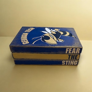 May include: A blue wooden box with a gold and black bee graphic and the words "GEORGIA TECH" and "FEAR THE STING" in white. The box has a distressed finish and a gold-colored edge.