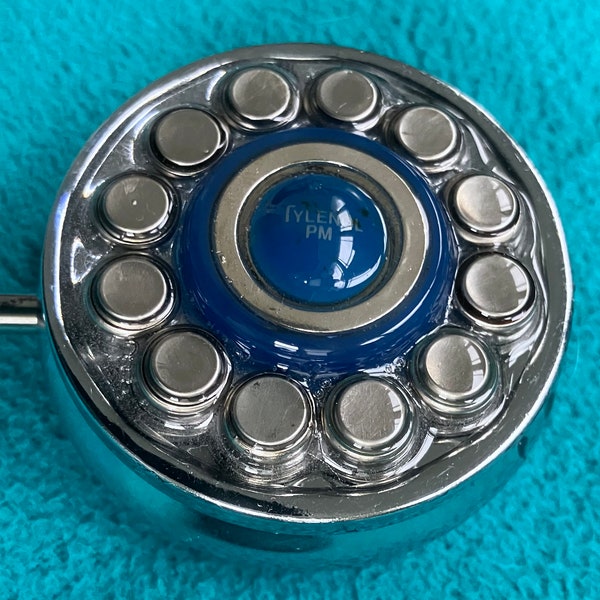 Petit silver metal pill box decorated with a royal blue Tylenol PM pill, a blue glass ring and 12 up-cycled hearing aid batteries