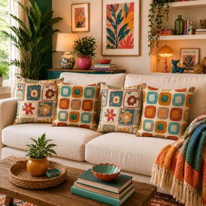May include: Four square throw pillows with colorful floral and geometric patterns rest on a white sofa. The pillows feature a mix of orange, blue, and yellow hues. A wooden coffee table holds a woven tray, a small plant, and books.
