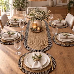 May include: A dining table setting featuring a long oval braided jute table runner with a black border, matching round braided jute placemats, white ceramic plates, linen napkins with jute rings, gold-toned flatware, and clear glassware.