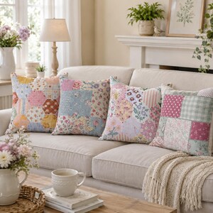 May include: Four decorative throw pillows with patchwork patterns in pastel colors, including pink, blue, yellow, and green. The pillows are arranged on a beige sofa, creating a cozy and inviting living room scene. Floral and geometric designs are visible.