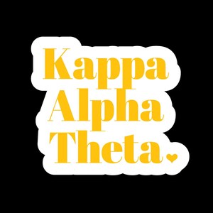 May include: A die-cut sticker featuring the text Kappa Alpha Theta in a bold, yellow serif font. The lettering is arranged in three lines with a small yellow heart icon at the end of the final word, all outlined in a thick white border.