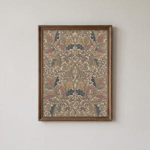 Può includere: Una stampa rettangolare incorniciata con un motivo botanico simmetrico di foglie di quercia e ghiande in tonalità tenui di blu, rosa, beige e verde su sfondo crema, racchiusa in una semplice cornice in legno marrone usurato.