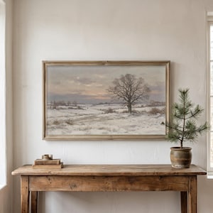 Könnte beinhalten: Ein rechteckiges gerahmtes Landschaftsgemälde, das ein schneebedecktes Feld mit einem großen, kahlen Baum unter einem weichen, gedämpften Himmel zeigt. Das Kunstwerk befindet sich in einem Holzrahmen über einem rustikalen Holzkonsolentisch.