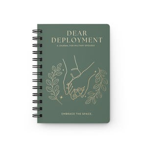 Può includere: Un diario a spirale color verde salvia con il testo DEAR DEPLOYMENT A JOURNAL FOR MILITARY SPOUSES e EMBRACE THE SPACE. La copertina presenta un'illustrazione a linee dorate di due mani che si tengono, circondate da rami frondosi.