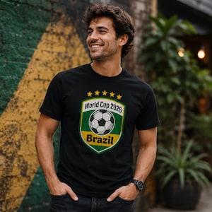 May include: Black t-shirt featuring a soccer ball design and the text "World Cup 2026 Brazil". The graphic is in green, yellow, and white. The shirt has short sleeves.