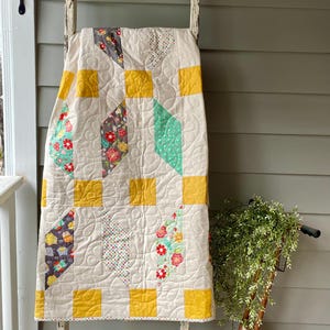 May include: A quilt featuring a cream-colored background with a repeating pattern of solid mustard yellow squares and diamond-shaped patches. The diamond patches display various floral, polka dot, and owl prints in shades of red, green, and gray.