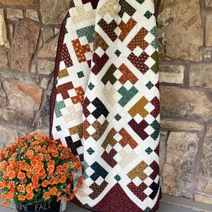 May include: A patchwork quilt featuring a geometric pattern of interconnected squares and rectangles in shades of burgundy, forest green, mustard yellow, and cream. The fabric pieces display various small-scale floral and abstract prints.