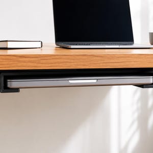 May include: A wooden desk with a black metal frame, with a laptop, a notebook, and a small succulent in a white pot. A laptop is stored on a black tray under the desk. A grey mug sits on the desk.