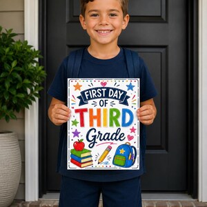 May include: A rectangular sign with the text First Day of Third Grade in colorful lettering. The design features illustrations of a red apple on a stack of books, a yellow pencil, and a blue backpack, surrounded by small colorful stars and hearts.