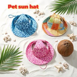 May include: Three pet sun hats in blue leopard print, a colorful patchwork design, and pink leopard print. The hats are displayed on a sandy surface with a coconut, coral, and palm leaves. The text "Pet sun hat" is at the top.