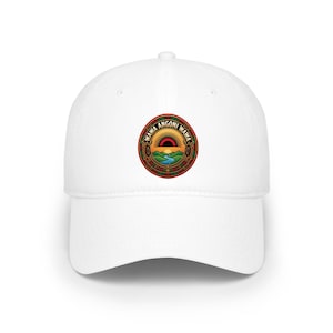 Peut inclure: Une casquette de baseball blanche avec un emblème circulaire sur le devant. L'emblème représente un lever de soleil sur des collines vertes et une rivière bleue, entouré d'une bordure décorative avec le texte WAWA ANGONI WAWA en lettres noires.