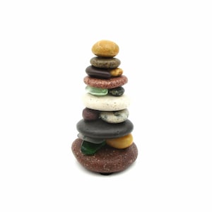 May include: A stack of smooth, colorful stones balanced on top of each other, creating a small tower. The stones are various shades of brown, red, white, and green.