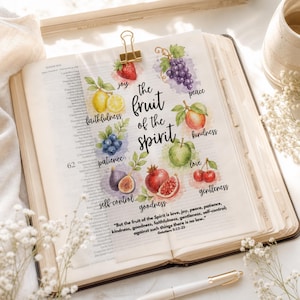 Könnte beinhalten: Ein aufgeschlagenes Buch mit einer Aquarellillustration verschiedener Früchte, die mit Tugenden beschriftet sind. Der Text lautet The fruit of the Spirit und enthält den Vers Galatians 5:22-23. Eine goldene Büroklammer hält die Seite.