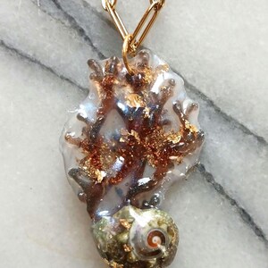 May include: A unique pendant necklace featuring a seahorse-shaped design. The pendant is made of clear resin with embedded gold flakes and brown accents. The seahorse is attached to a gold chain.