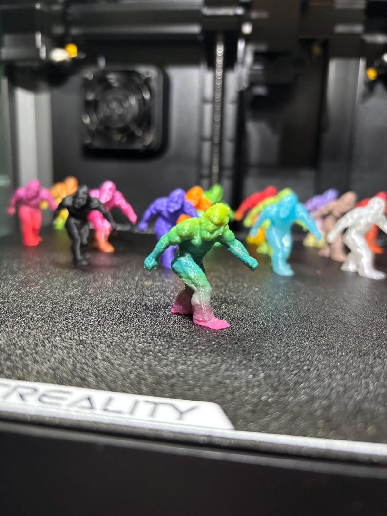 May include: A collection of small, 3D-printed humanoid figurines in various solid and gradient colors, including a prominent foreground figure featuring a green-to-pink color transition, all standing in a crouched, forward-leaning pose.