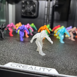 May include: A collection of small, 3D-printed humanoid figurines in various colors, including translucent, purple, pink, orange, green, blue, and black. The figures are in a dynamic, crouching pose. The word CREALITY is printed on the surface.