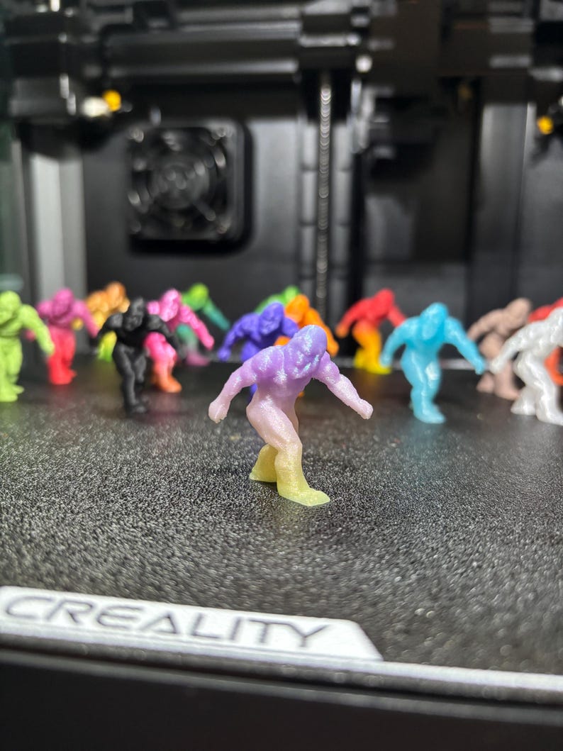 May include: A collection of small, 3D-printed humanoid figurines in various solid and gradient colors, including purple, yellow, blue, black, and pink. Each figure is in a dynamic, crouching pose with arms extended. The word CREALITY is visible.