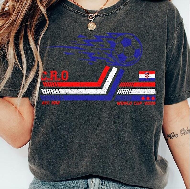 May include: Dark gray t-shirt featuring a soccer ball graphic with blue flames. The shirt includes the text "CRO" and "WORLD CUP 2026" with the Croatian flag design. The shirt also has the text "EST. 1912".