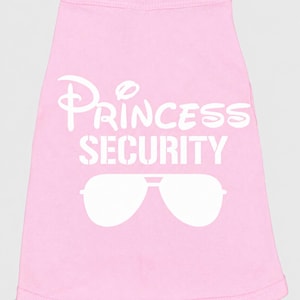 May include: A light pink sleeveless pet shirt featuring the white text "PRINCESS SECURITY" printed in a stylized font, accompanied by a graphic of white aviator-style sunglasses positioned directly below the text on the front of the garment.
