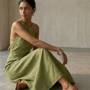 May include: A sleeveless olive green maxi dress with a high neckline and an open back design, paired with tan brown leather sandals featuring a braided strap detail across the top of the foot and a simple toe loop construction.
