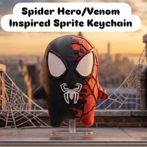 May include: A dual-colored keychain featuring a character design split between black and red with a white spider emblem on the chest and large white eyes. The text above reads Spider Hero/Venom Inspired Sprite Keychain in black lettering.