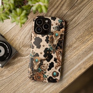 a phone case with a floral and skull design, placed on a wooden surface next to a camera.