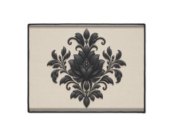 May include: A rectangular mat featuring a beige background with a central black damask floral motif. The design includes a symmetrical arrangement of stylized leaves and petals. The mat is framed by thin black horizontal lines along the top and bottom edges.