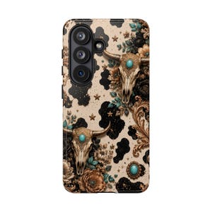 May include: A phone case featuring a beige and black cow print background decorated with two steer skulls, each adorned with a central turquoise stone. The design includes brown floral accents, gold filigree patterns, and small gold stars.