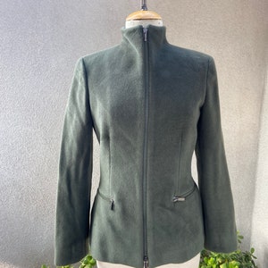 May include: A dark green, zippered jacket with a high collar. The jacket has a fitted silhouette and two zippered pockets on the sides.