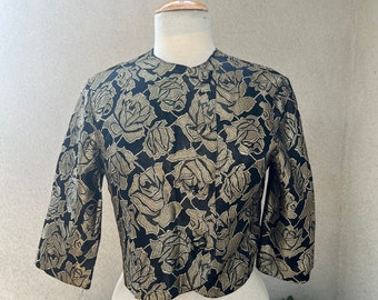 May include: A black and gold cropped jacket with a rose pattern. The jacket has a round neckline and three-quarter sleeves.