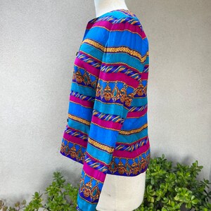 May include: A long-sleeved, blue, pink, and gold striped blouse with a patterned design. The blouse has a button-up front and a fitted silhouette.