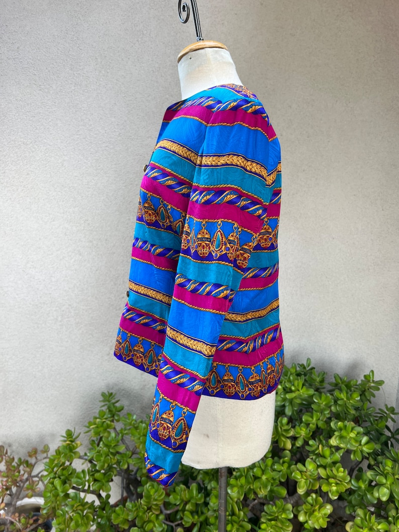 May include: A long-sleeved, blue, pink, and gold striped blouse with a patterned design. The blouse has a button-up front and a fitted silhouette.