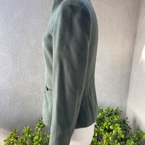 May include: A dark green, zip-up jacket with a stand-up collar. The jacket is made of a soft, fuzzy fabric.