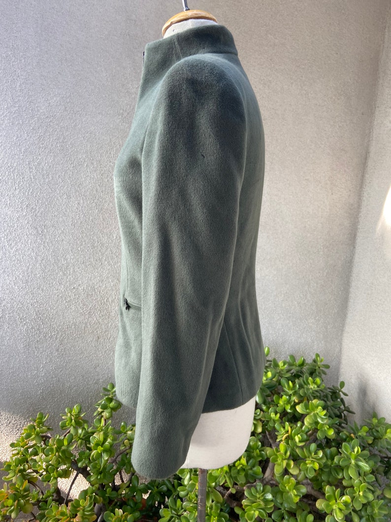 May include: A dark green, zip-up jacket with a stand-up collar. The jacket is made of a soft, fuzzy fabric.