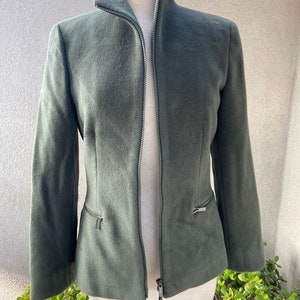 May include: A dark green, zippered jacket with a high collar. The jacket has two zippered pockets on the sides.