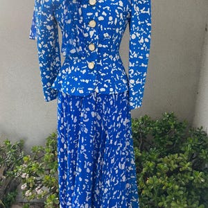 May include: A blue and white patterned skirt suit with a white bow tie. The suit has a fitted jacket with a cinched waist and a long skirt.