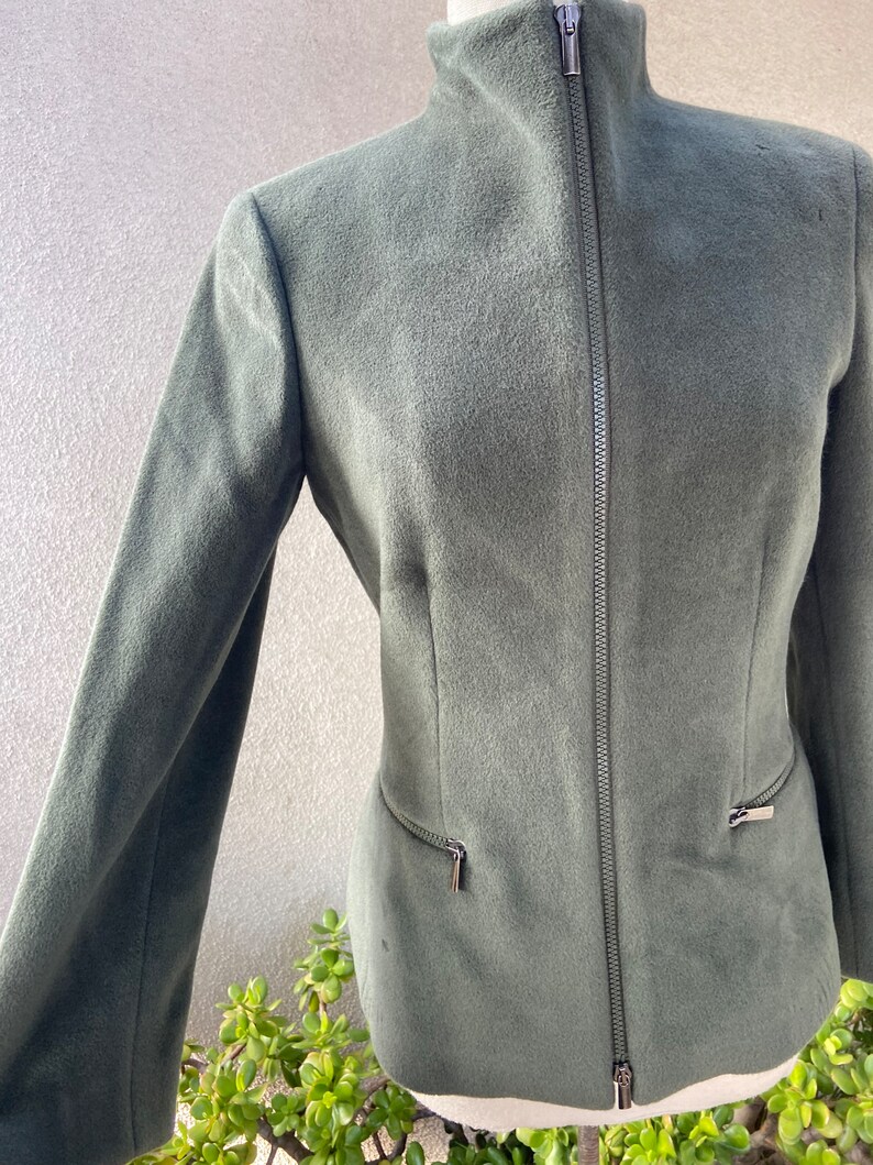 May include: A dark green zip-up jacket with a high collar and two zippered pockets on the sides.