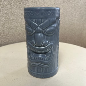 May include: A gray ceramic tiki mug with a carved face and a geometric pattern around the top and bottom.