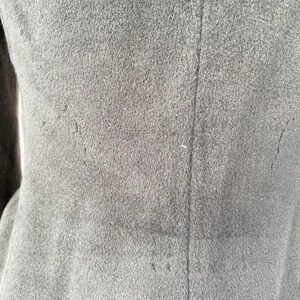 May include: Close-up of the back of a gray wool coat. The coat has a seam down the center back and two seams on either side of the center seam. The seams are visible because they are stitched with a contrasting thread.