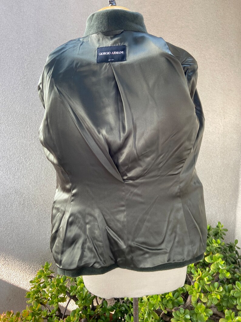 May include: A dark green blazer with a satin lining. The label on the inside reads "Giorgio Armani" in black text.