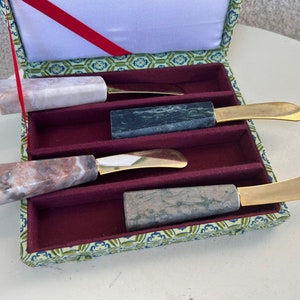May include: Set of four marble and gold butter knives in a green and gold box. The knives have different colored marble handles and gold blades.