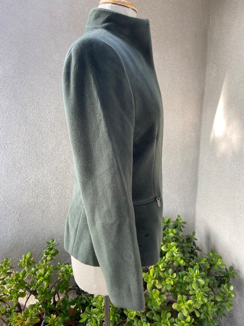 May include: A dark green, long-sleeved jacket with a high collar and a zipper closure. The jacket has a slim fit and is made of a soft, textured fabric.