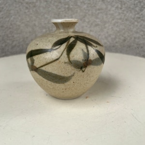 May include: A small, cream-colored ceramic vase with a brown and green leaf design.