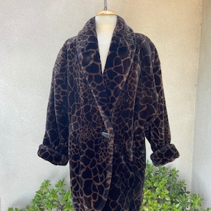 Puede incluir: Una chaqueta de piel sintética marrón y negra con estampado de leopardo. La chaqueta tiene un cuello chal y un cierre de botón único.