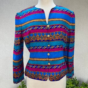 May include: A blue, pink, and gold striped blouse with a button-up front and a geometric pattern. The blouse has long sleeves and a v-neck.