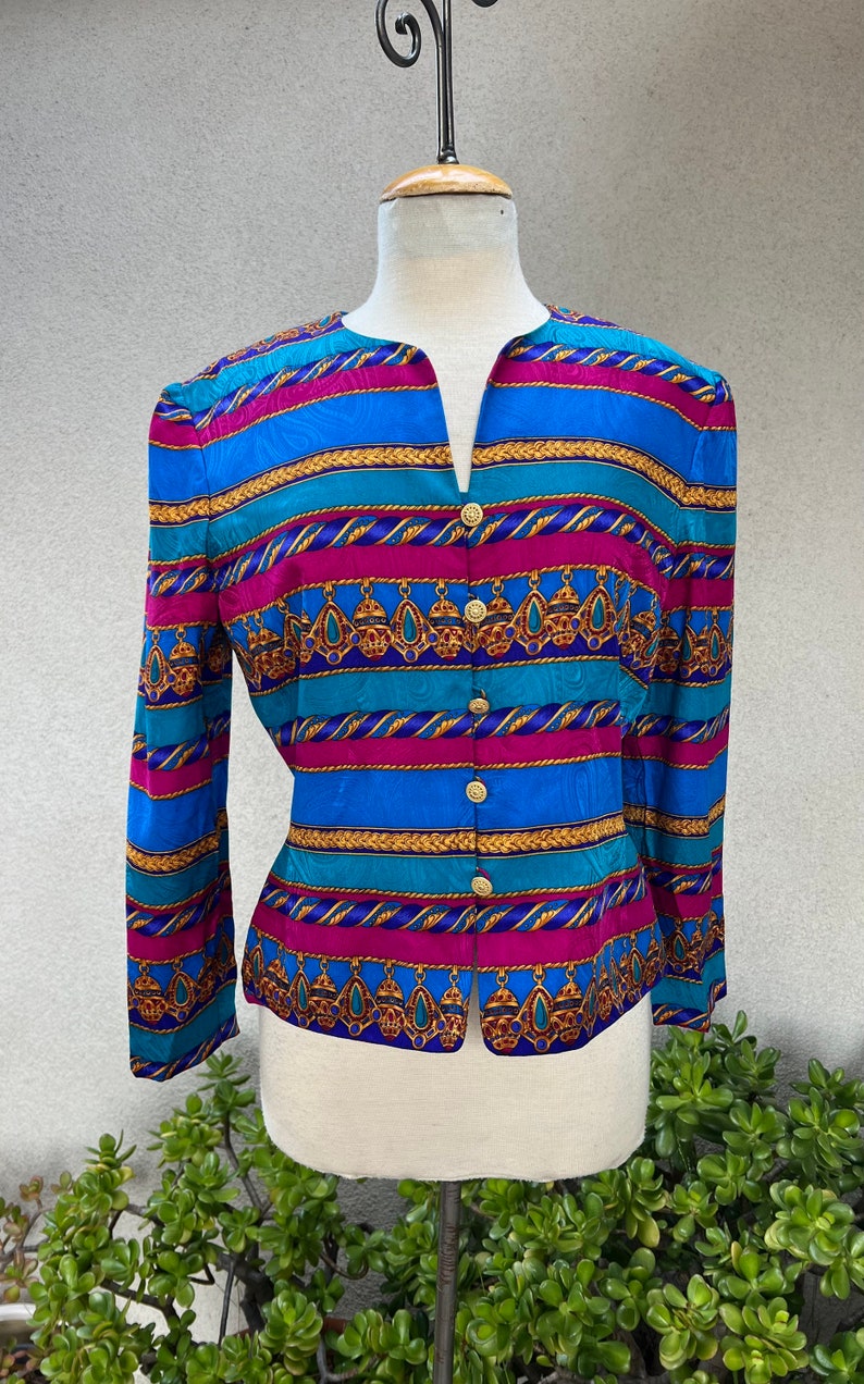 May include: A blue, pink, and gold striped blouse with a button-up front and a geometric pattern. The blouse has long sleeves and a v-neck.