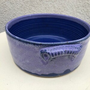 May include: A purple and blue ceramic baking dish with a single handle. The dish has a textured, speckled glaze.