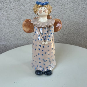 May include: A ceramic angel figurine with a light brown dress with blue polka dots, brown wings, and a blue bow in her hair.